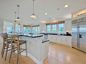 A modern kitchen with a central island, bar stools, pendant lighting, and a stainless steel refrigerator.