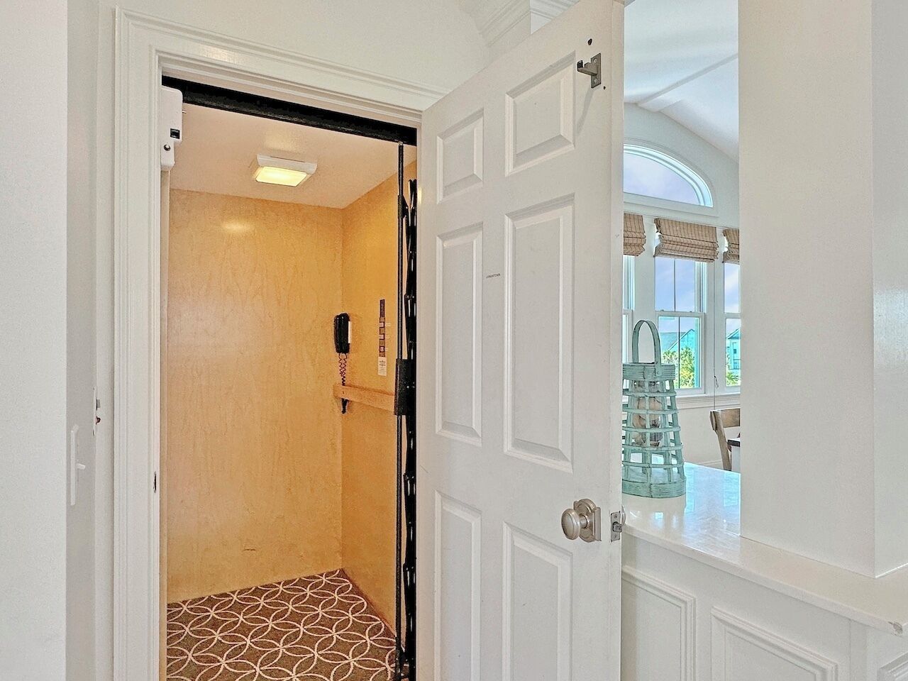 A room with a patterned floor, a door leading to another room, and a window with a view of the outside.