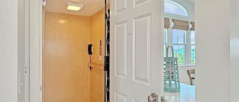 A room with a patterned floor, a door leading to another room, and a window with a view of the outside.