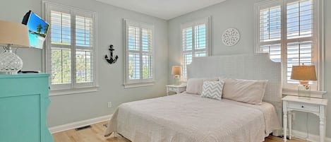 A bedroom with a bed, a ceiling fan, a TV, and a window with shutters.