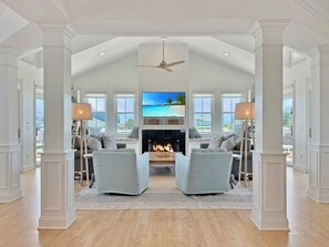 A spacious living room with a fireplace, two armchairs, and a television displaying a beach scene.