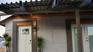 A modern building entrance with a white door, two potted plants, a welcome mat, and a covered porch area. - Private Guesthouse in Central Phx--Beaker Bunker (Phoenix)