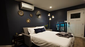 A modern bedroom with a bed, bedside tables, a nightstand, a mirror, wall decorations, and an air conditioning unit. - Private Guesthouse in Central Phx--Beaker Bunker (Phoenix)