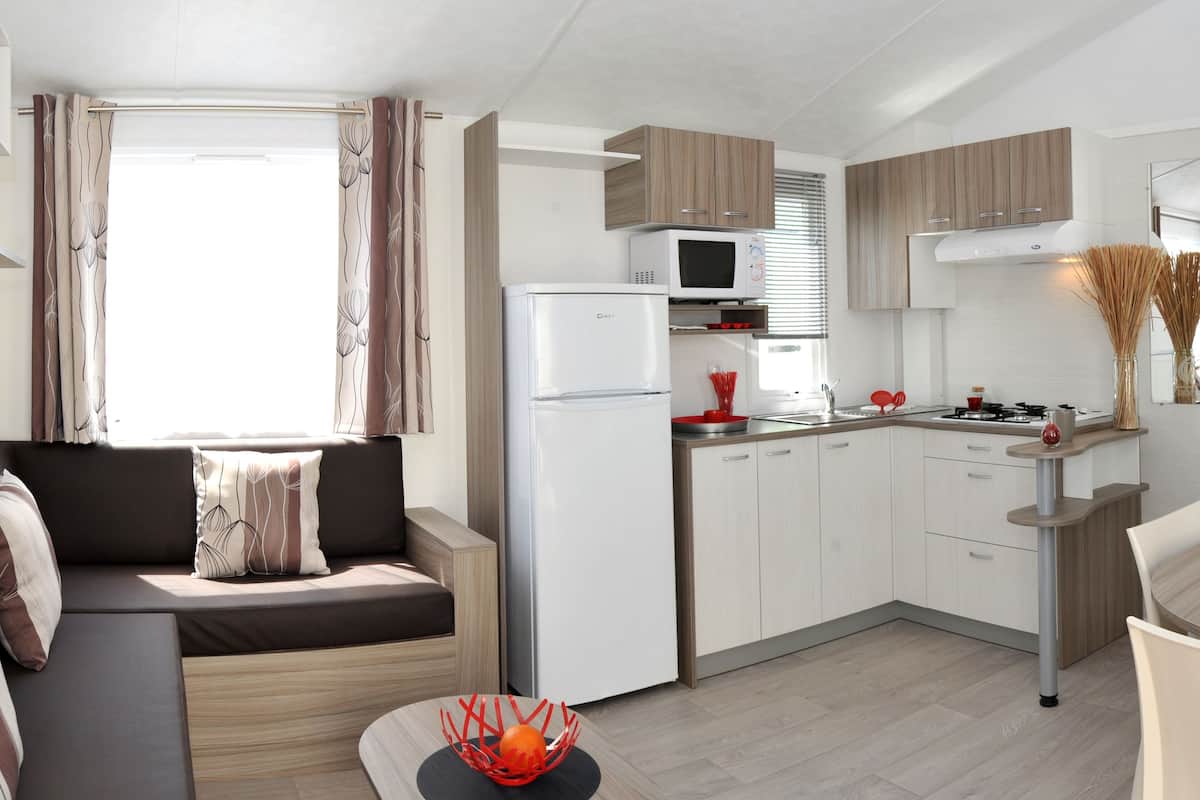 A compact kitchen with a microwave, stove, and sink. There is a dining table with chairs and a sofa with cushions.