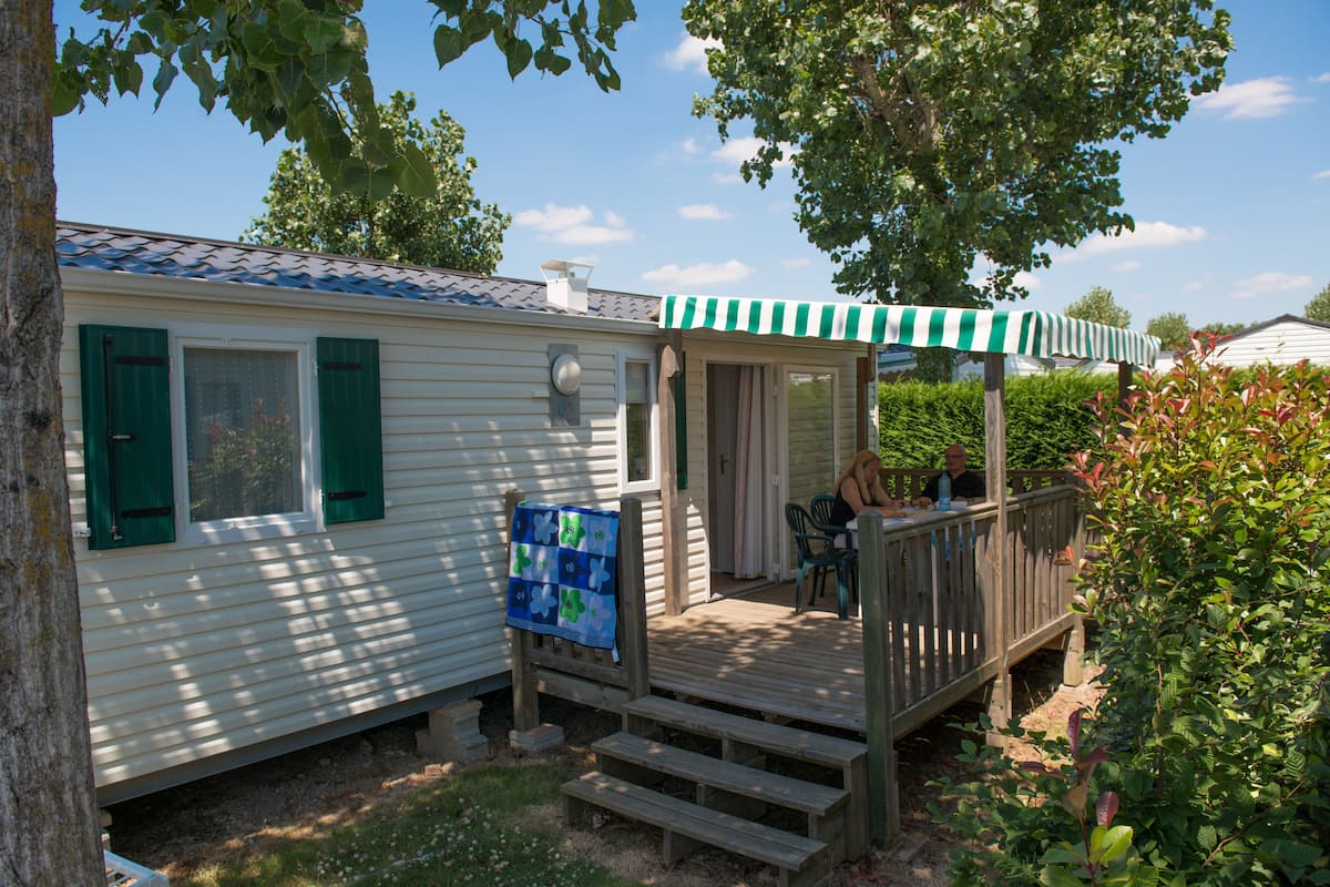 A mobile home with a porch, a covered outdoor seating area, and a small deck.