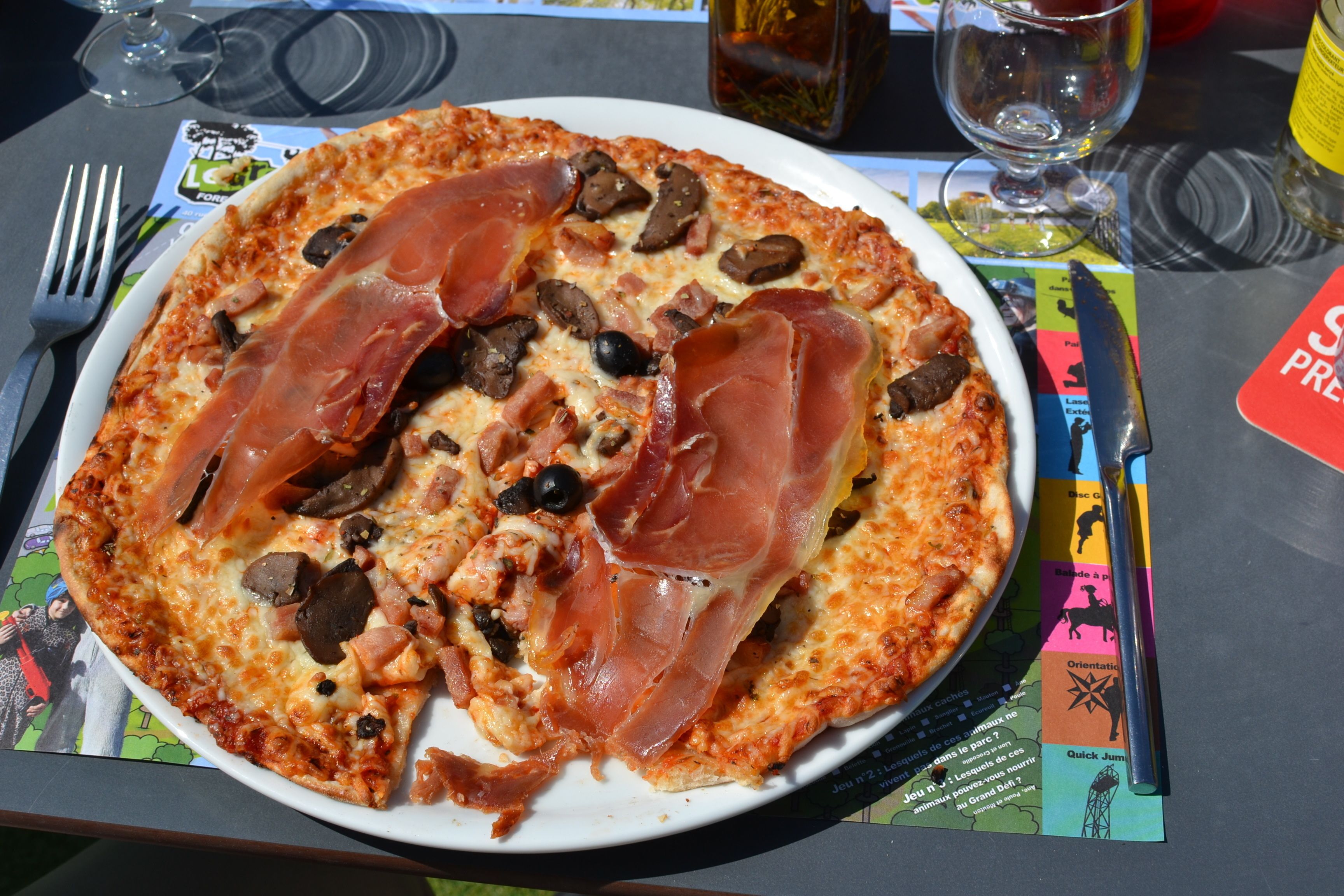 A pizza with ham and olives on a white plate.