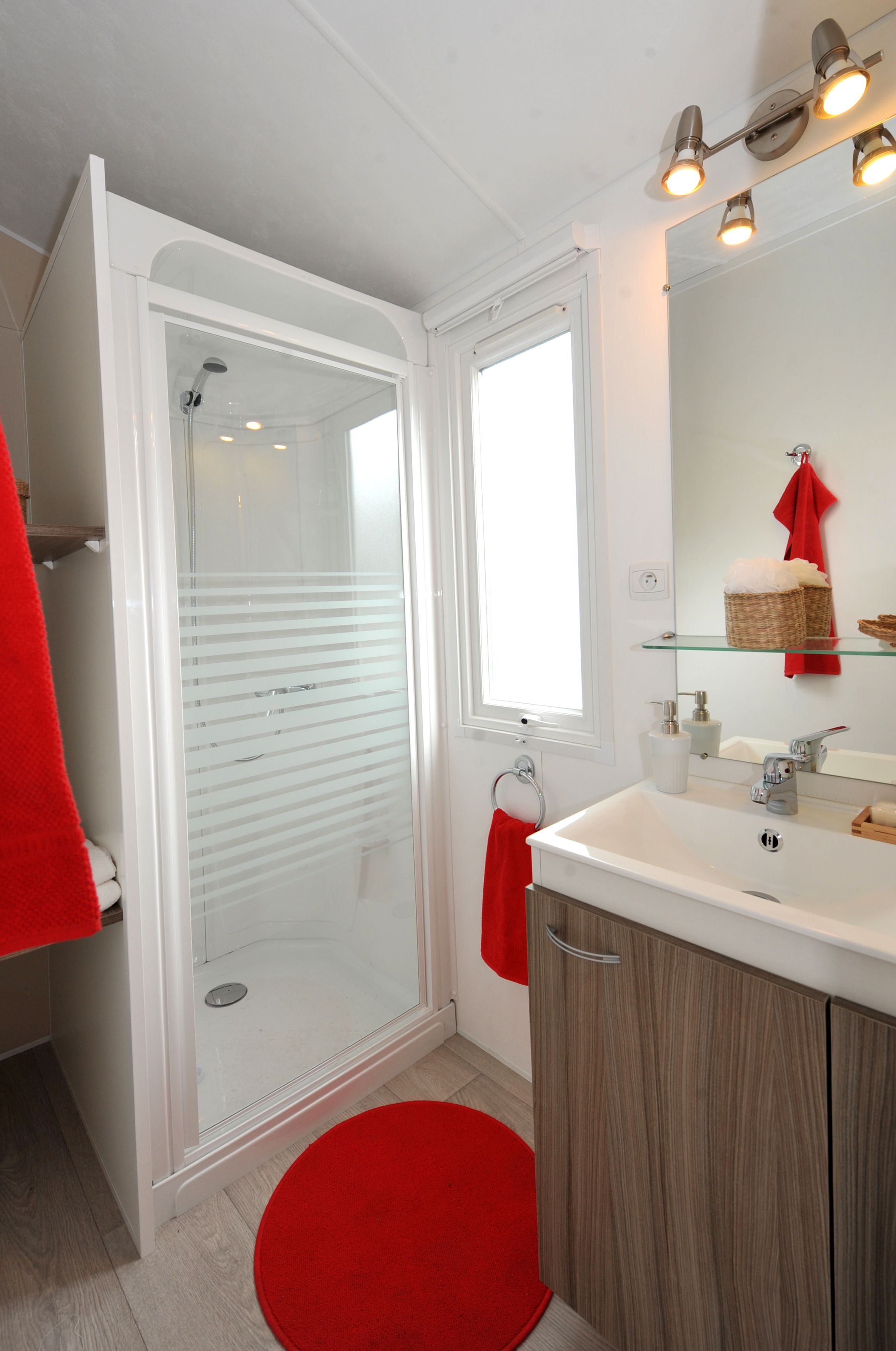 A bathroom with a glass-enclosed shower, a white sink with a mirror, and a red towel on the floor.