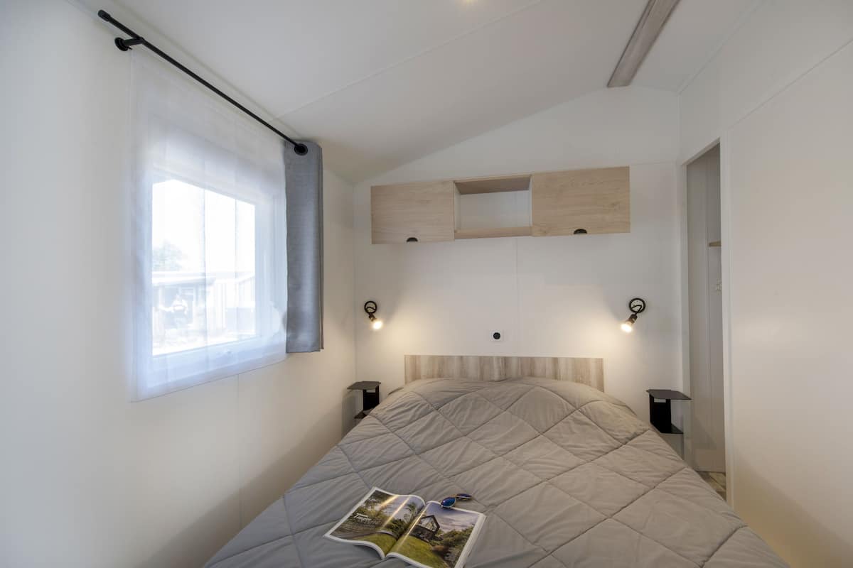 A bedroom with a bed, a window with curtains, bedside tables, and built-in shelves.