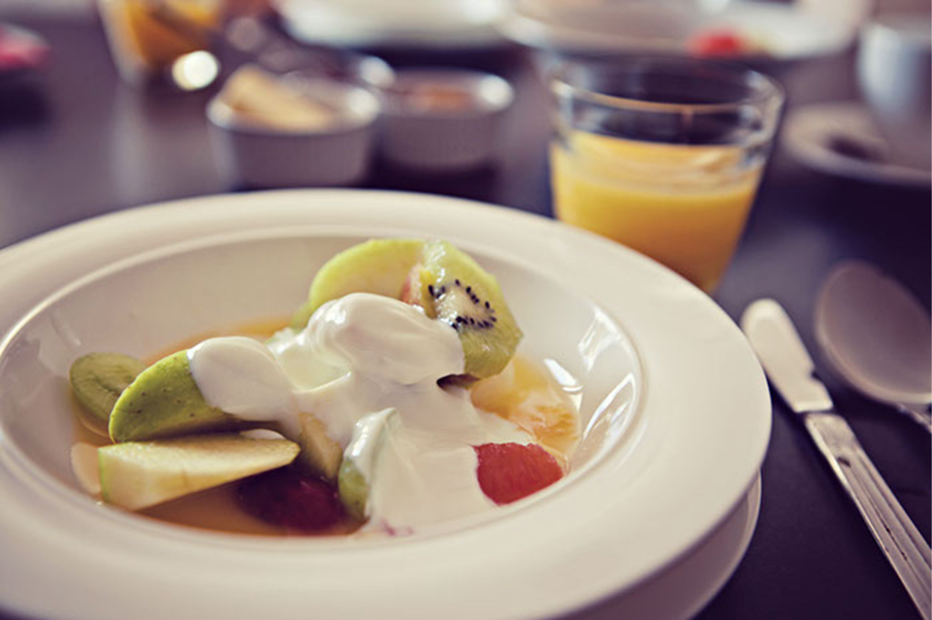Un plato de fruta con yogur y un vaso de zumo de naranja sobre una mesa.