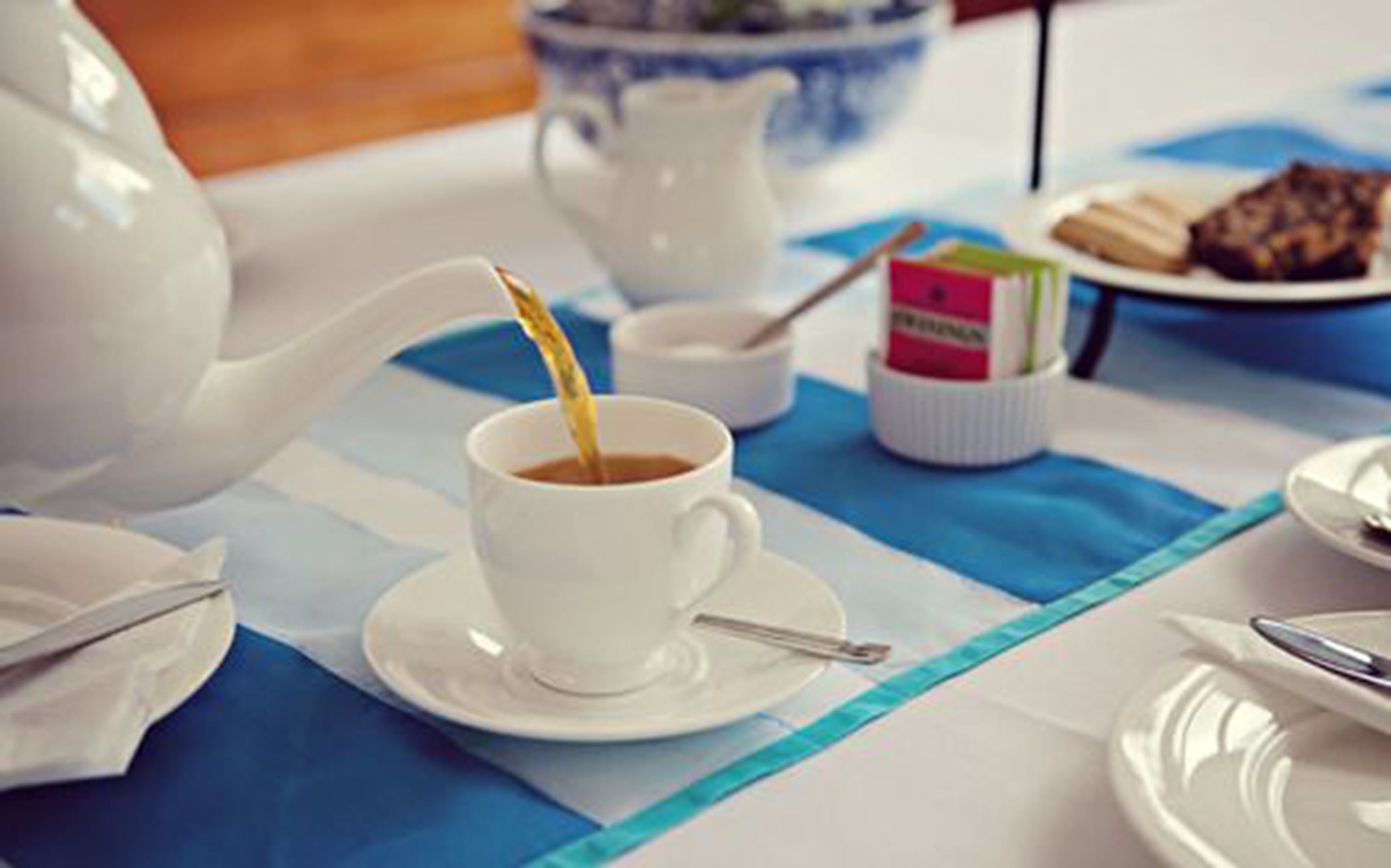 A table with a white teapot, a cup of tea, a small bowl, and a plate with pastries.
