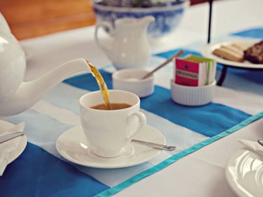 A table with a white teapot, a cup of tea, a small bowl, and a plate with pastries.