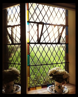 A window with a metal grid, a white vase with a floral design, and a wooden table.