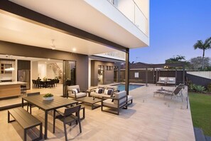 Ein moderner Außenbereich mit Pool, Sitzgelegenheiten und einer durch Glastüren einsehbarer Küche.