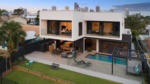 Ein modernes, zweistöckiges Haus mit Pool, Sitzgelegenheit im Freien und Blick auf die Stadtlandschaft.