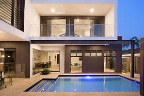 Ein modernes, zweistöckiges Haus mit Schwimmbad, großen Glasfenstern und einem Balkon.