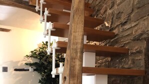 Un interior modern amb una escala de fusta, una cadira tapissada de gris i una taula amb llibres i una planta.
