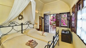 A bedroom with two beds, a canopy bed, a small table with a plant, and a view of pink flowers through an open door. - VILLA DEUS (Santorini,Thira)