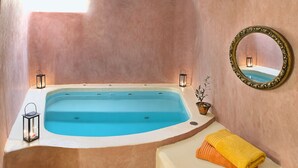 A spa room with a bathtub, two lanterns, a mirror, and a towel on a counter. - VILLA DEUS (Santorini,Thira)