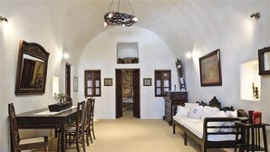 A room with a dining table, chairs, a bed, and a staircase leading to an upper level. - VILLA DEUS (Santorini,Thira)