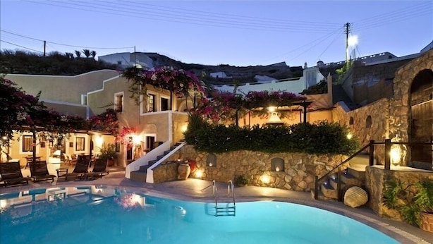 A swimming pool with lounge chairs, a stone wall, and a staircase leading to a second floor. - VILLA DEUS (Santorini,Thira)