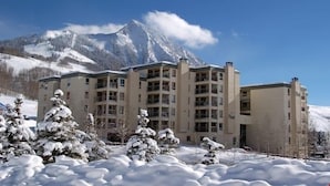 Ein mehrstöckiges Hotel vor einer verschneiten Landschaft und Bergen im Hintergrund.
