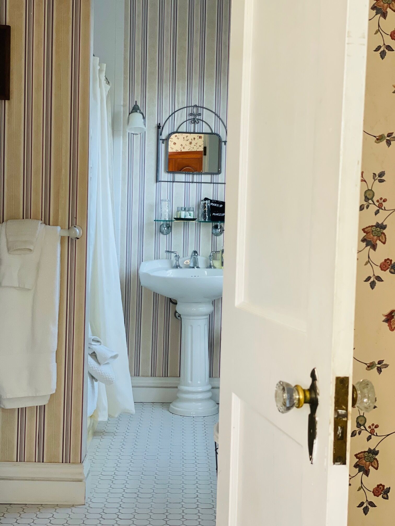 Un baño con papel tapiz a rayas, un lavamanos pedestal, un espejo y un toallero.