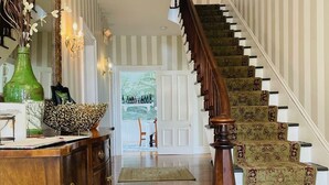 A wooden staircase with patterned carpet, a wooden cabinet with drawers, a green vase, and a mirror. - Langworthy Inn (Westerly)