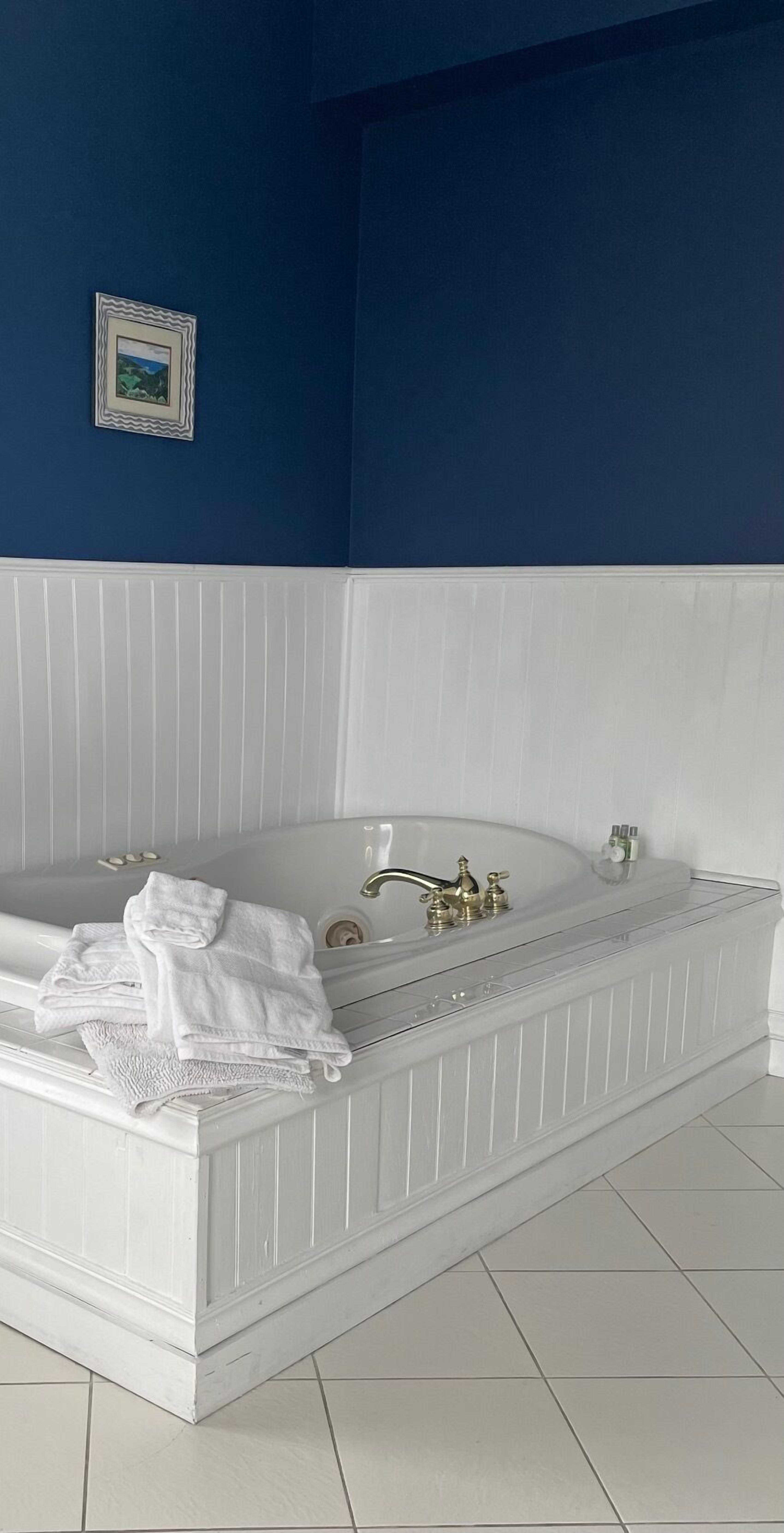 A white freestanding bathtub with a white base, a single faucet, and a small shelf with toiletries.
