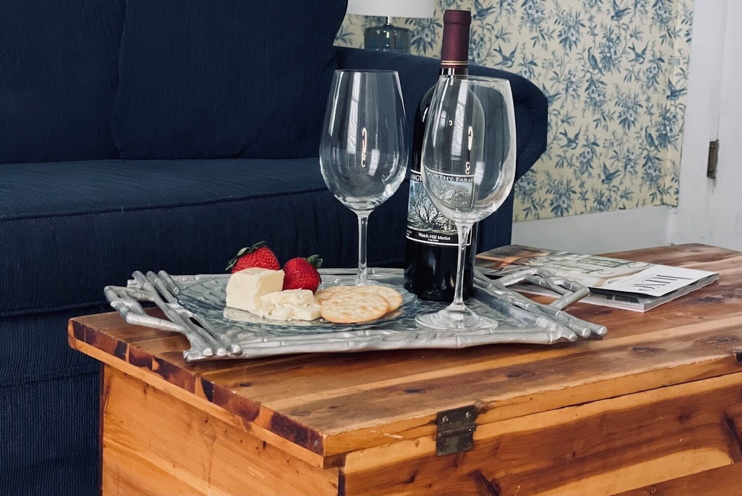 Uma mesa de madeira com uma bandeja que contém queijo, morangos e uma garrafa de vinho.
