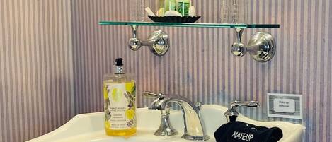 A bathroom with a white pedestal sink, a glass shelf above the sink, and a mirror with a decorative frame.