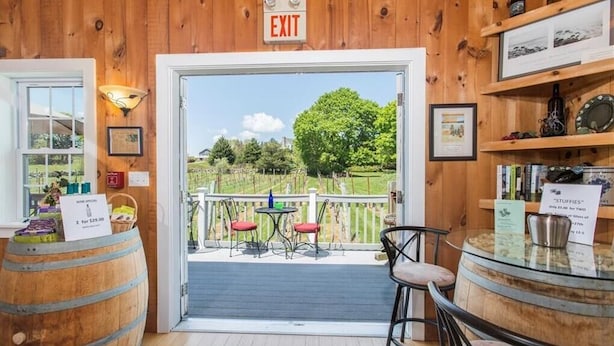 A wooden interior with an exit sign, a view of a vineyard, and a bar area with stools and a round table. - Langworthy Inn (Westerly)