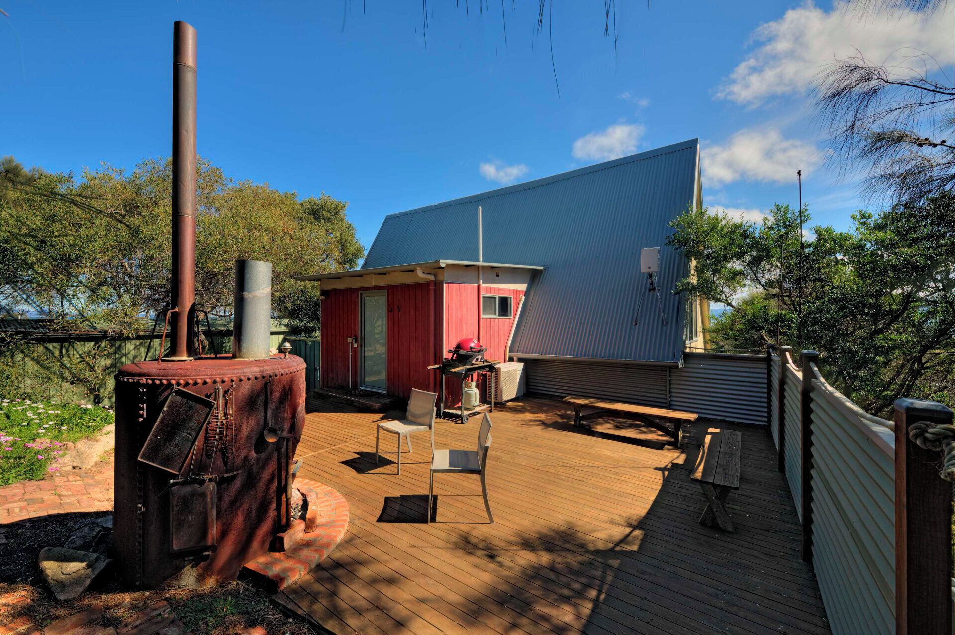A rustic outdoor deck with a metal grill, a red building, and a large blue structure.