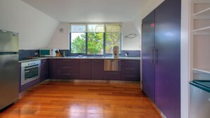 A kitchen with wooden flooring, a window with a view of trees, a purple cabinet, and a microwave.