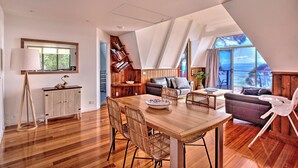 A spacious living area with a wooden dining table, two sofas, and a large window offering a view of the sea.