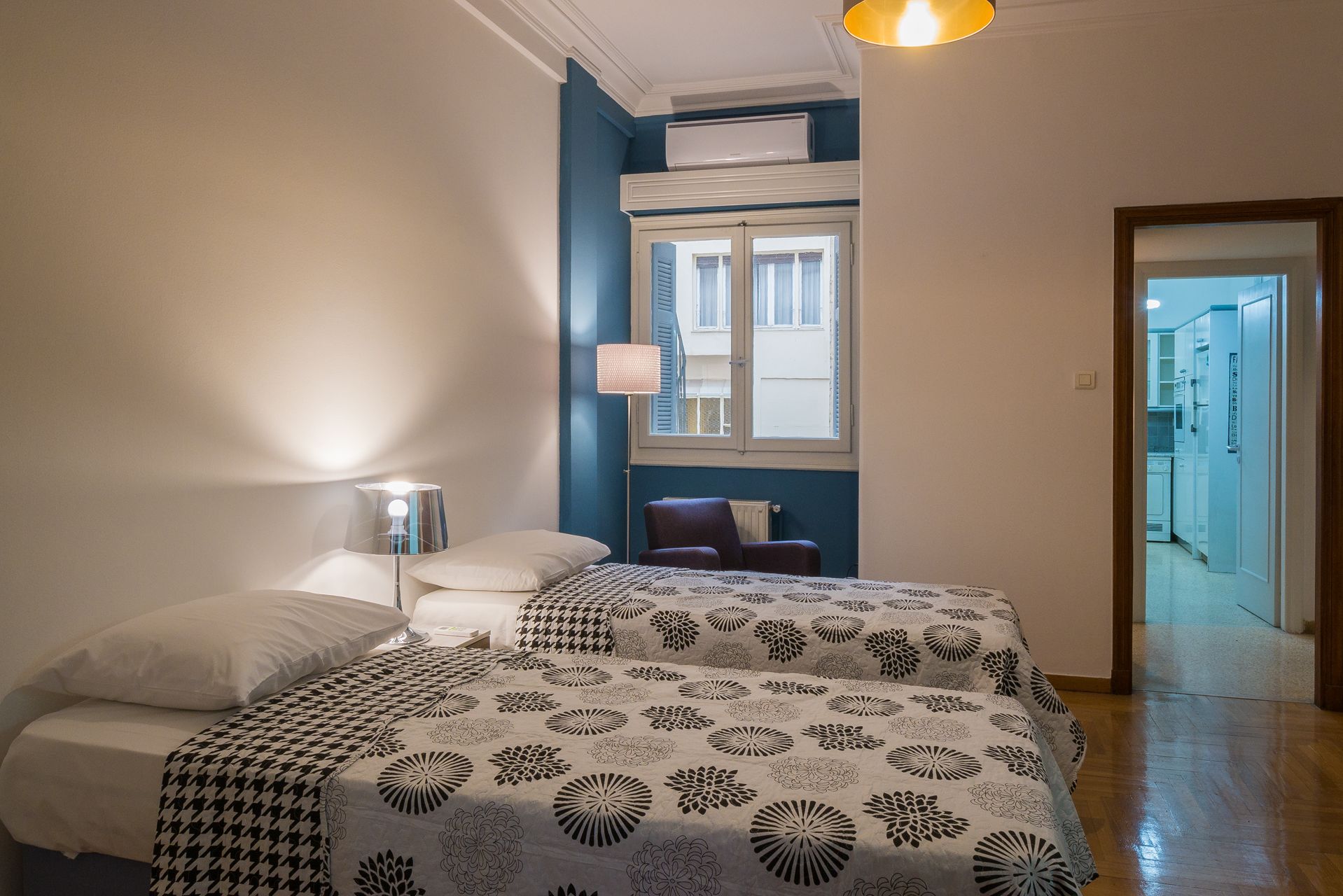 Ein Schlafzimmer mit zwei Betten, einem Fenster mit Rollläden, einer Klimaanlage und einer Lampe.