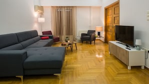 Een moderne woonkamer met een bank, fauteuils, een televisie en een houten vloer.