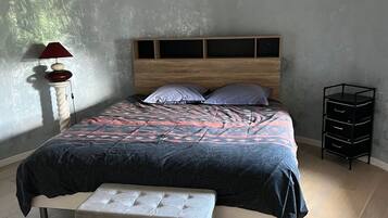 Ett sovrum med en säng, en bänk, ett sängbord, en lampa och en liten svart förvaringsmöbel.