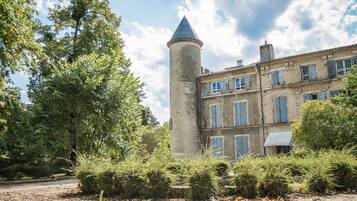 A historic building with a tower, surrounded by lush greenery and a gravel path.
