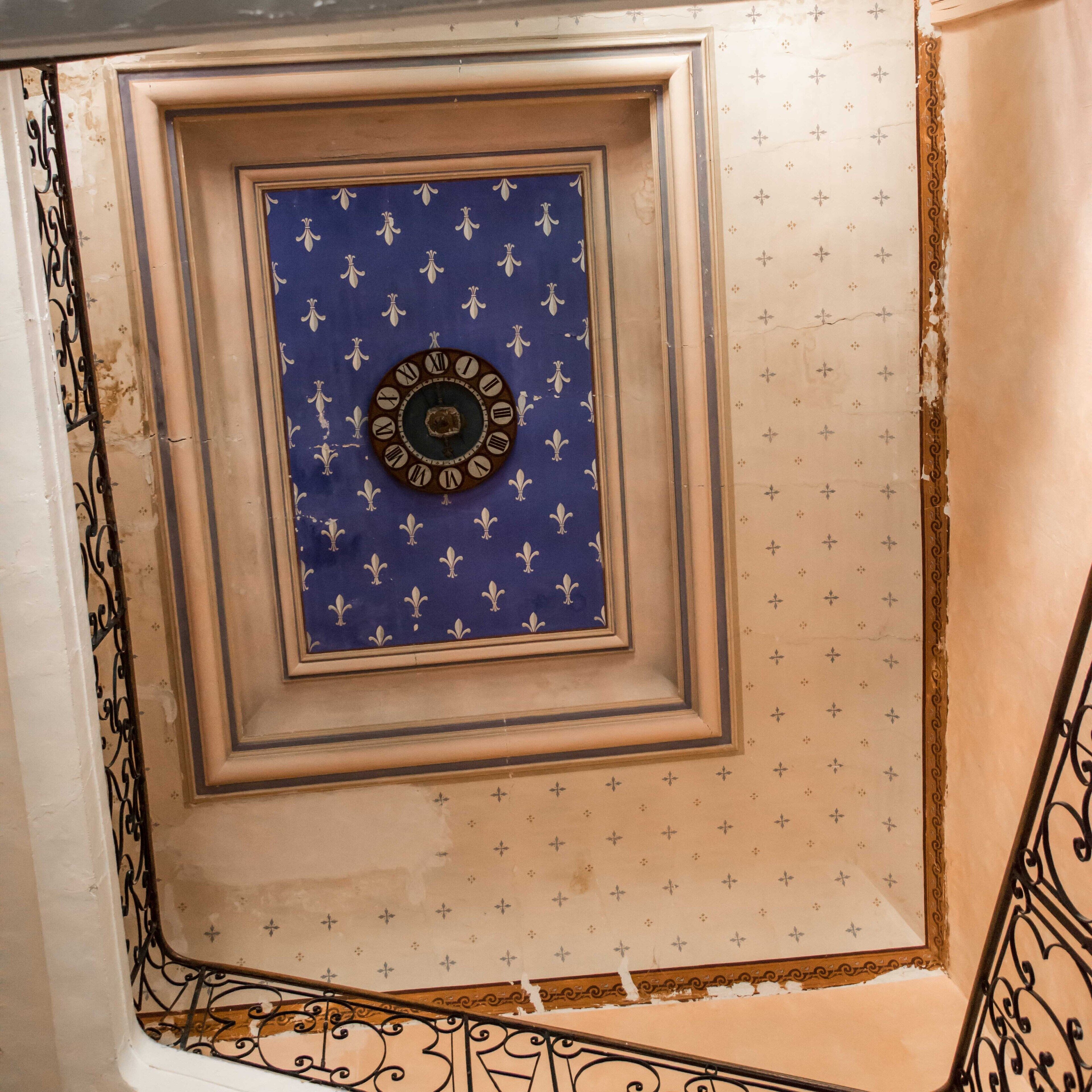 Una escalera con barandillas de metal ornamentadas y un techo decorativo que incluye un reloj.