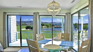 A balcony with a glass table, chairs, and a view of a lake and mountains.