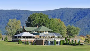 A large building with a green roof and multiple covered areas, surrounded by a well-maintained lawn and trees, with a mountainous backdrop.