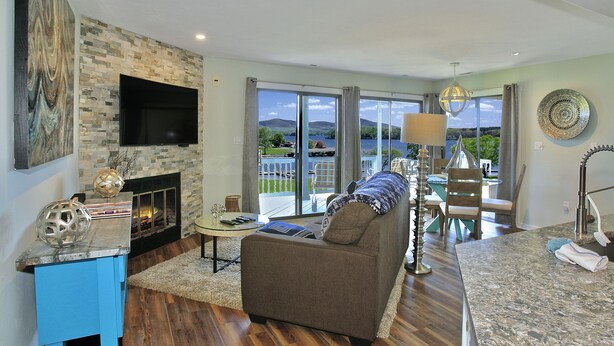 A spacious living room with a fireplace, a large flat-screen TV, and a view of the outdoors.