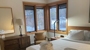 Ein Hotelzimmer mit einem großen Bett, einer Holzkommode, einem Stuhl, einem Schreibtisch und einem Fenster mit Blick auf Bäume.