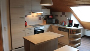 Eine moderne Küche mit Kochinsel, integrierten Geräten und einer schrägen Decke mit Oberlicht.
