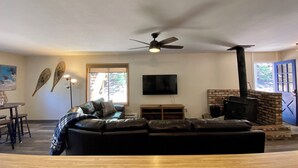 Ein Wohnzimmer mit schwarzem Ledersofa, einem Flachbildfernseher, einem Kamin und einem Deckenventilator.