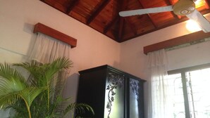 Une pièce avec un plafond en bois, un ventilateur de plafond, un meuble sombre en bois et une grande plante.