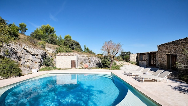 A swimming pool with lounge chairs, a stone building, and a rocky hillside. - Provencal farmhouse in central Provence (Caumont-Sur-Durance)