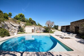 A swimming pool with lounge chairs, a stone building, and a rocky hillside. - Provencal farmhouse in central Provence (Caumont-Sur-Durance)