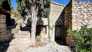 A stone building with a narrow entrance, a wooden door, and a staircase leading up. - Provencal farmhouse in central Provence (Caumont-Sur-Durance)