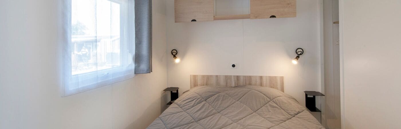 A bedroom with a bed, two bedside lamps, a window with a curtain, and a wooden headboard.